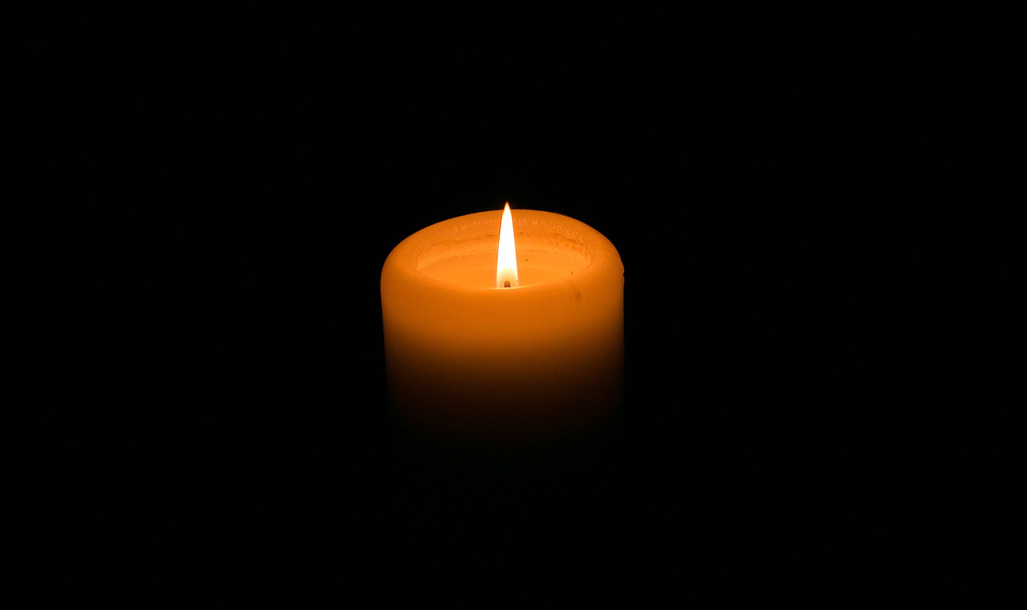 A candle with a tall flame in the dark.